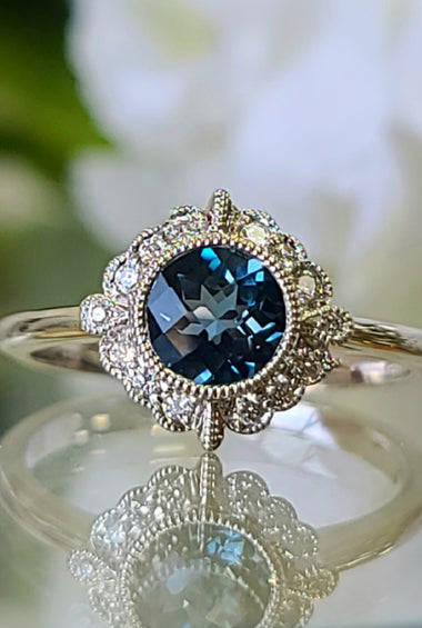 White gold ring with round blue topaz center and diamond halo