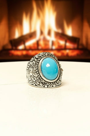 Silver ring with a turquoise stone in front of a fireplace