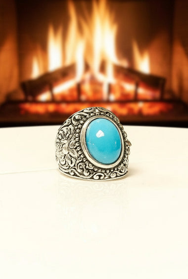 Silver ring with a turquoise stone in front of a fireplace