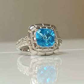 Sterling silver ring with cushion-cut blue topaz gemstone in ornate halo setting