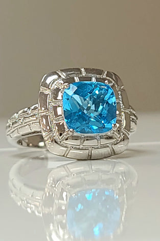 Sterling silver ring with cushion-cut blue topaz gemstone in ornate halo setting