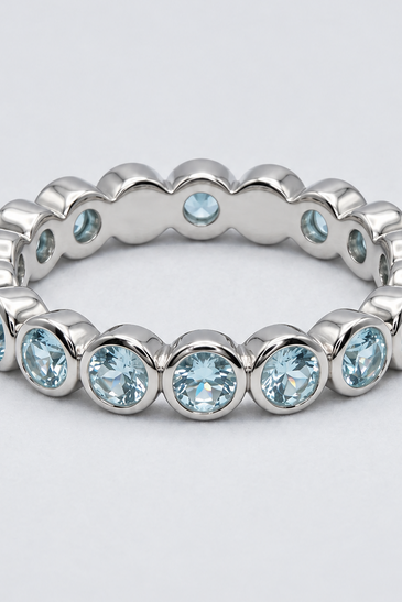 A sterling silver eternity ring featuring a continuous row of bezel-set light blue round gemstones.