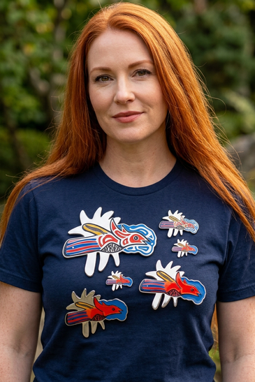 A woman with long red hair wearing a navy blue t-shirt with colorful embroidered bird designs.