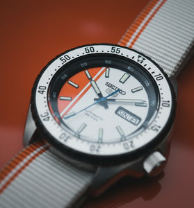 Seiko SRPK73 wristwatch with orange-and-white dial, black bezel, striped fabric strap