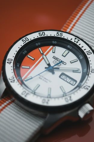 Seiko SRPK73 wristwatch with orange-and-white dial, black bezel, striped fabric strap