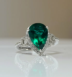 pear cut lab grown emerald surrounded by diamonds with a 10k white gold band