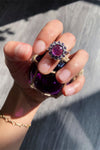 On the sterling silver ring, a violet cabochon stone is held together by mini amethyst gems